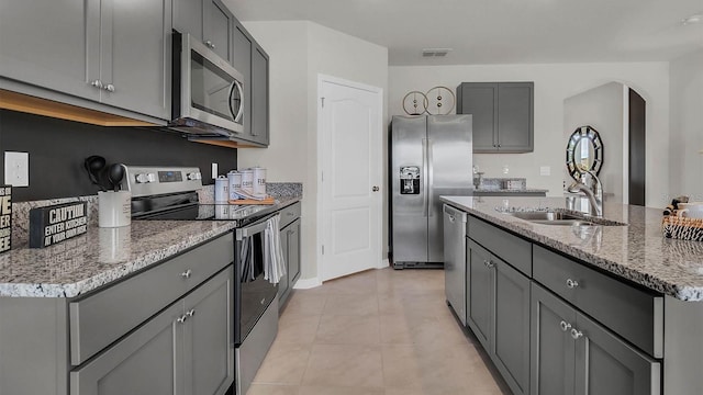 kitchen featuring appliances with stainless steel finishes, gray cabinetry, light tile patterned flooring, an island with sink, and sink