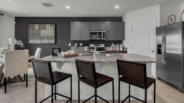 kitchen with light stone counters, sink, an island with sink, gray cabinetry, and stainless steel appliances