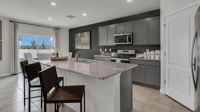 kitchen featuring gray cabinetry, stainless steel appliances, a kitchen breakfast bar, and a kitchen island with sink