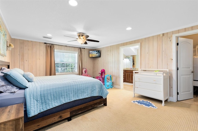 bedroom featuring light carpet, wooden walls, connected bathroom, and ceiling fan