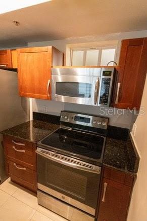 kitchen with dark stone countertops, appliances with stainless steel finishes, and light tile patterned floors