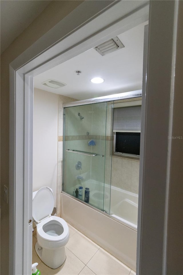 bathroom with tile patterned flooring, shower / bath combination with glass door, and toilet