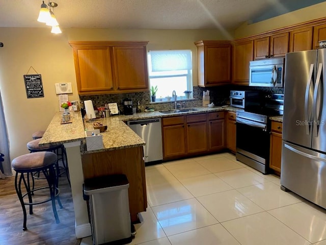 kitchen featuring kitchen peninsula, stainless steel appliances, backsplash, sink, and vaulted ceiling