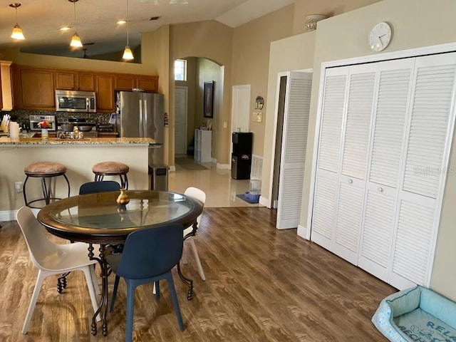 kitchen with kitchen peninsula, dark hardwood / wood-style flooring, appliances with stainless steel finishes, light stone countertops, and decorative light fixtures