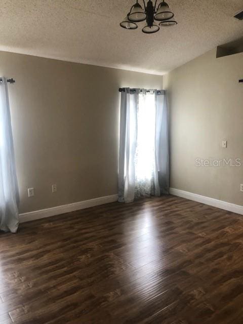 spare room with a textured ceiling, a chandelier, and dark hardwood / wood-style floors