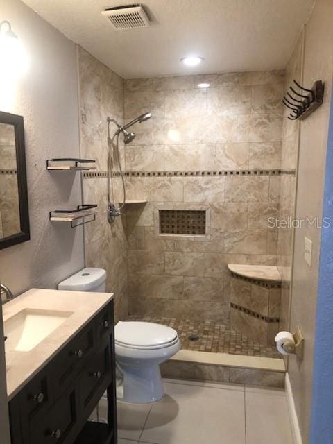 bathroom featuring vanity, a tile shower, toilet, and tile patterned floors