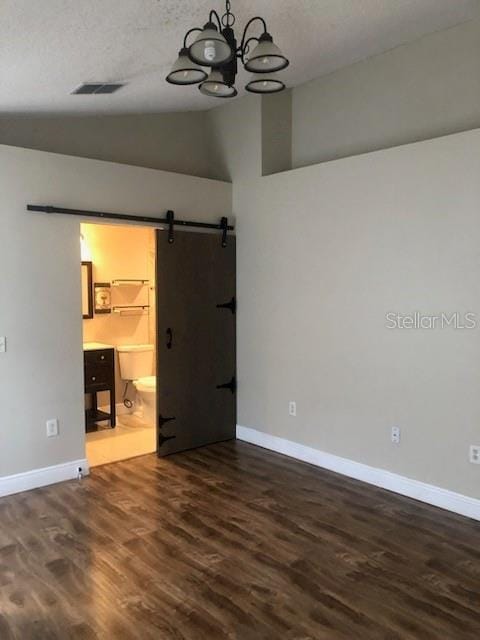 spare room with a chandelier, vaulted ceiling, dark hardwood / wood-style floors, and a barn door