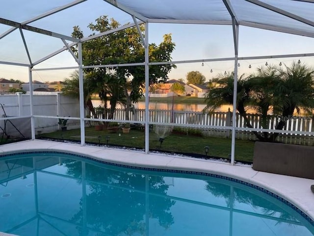 pool at dusk with a water view, a lawn, and a lanai