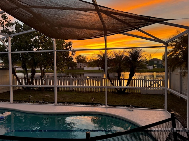 pool at dusk featuring a water view, a patio, a lanai, and a lawn