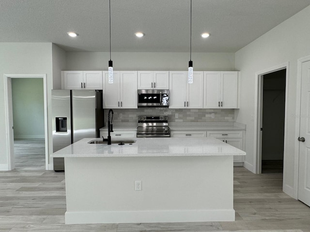 kitchen with a kitchen island with sink, sink, white cabinets, hanging light fixtures, and stainless steel appliances