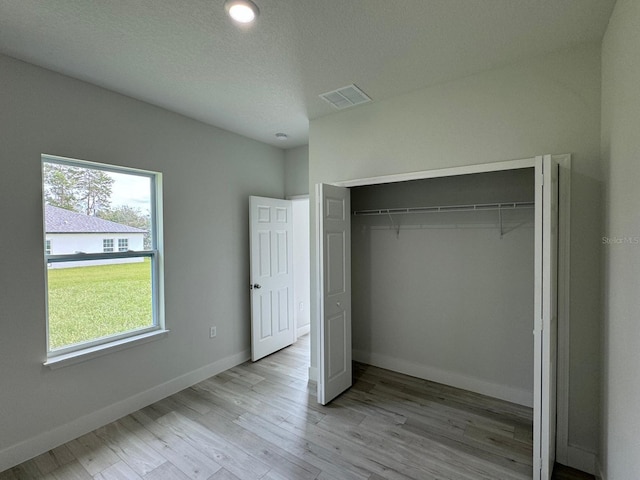 unfurnished bedroom featuring a textured ceiling, a closet, and light wood-type flooring