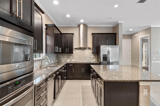 kitchen with light stone countertops, a center island, stainless steel appliances, sink, and wall chimney range hood