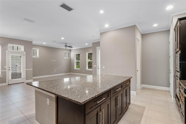 kitchen with light stone countertops, ceiling fan, a center island, ornamental molding, and light tile patterned floors