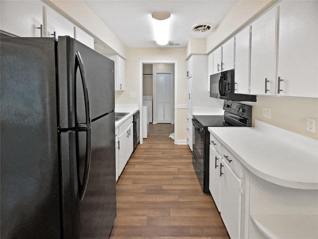 kitchen with black appliances, independent washer and dryer, white cabinetry, and hardwood / wood-style floors