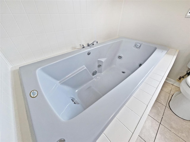 bathroom with tile patterned flooring, tiled bath, and toilet