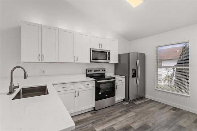 kitchen with sink, stainless steel appliances, wood-type flooring, white cabinets, and vaulted ceiling