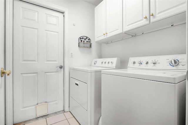 clothes washing area featuring cabinets, light tile patterned floors, and washing machine and dryer