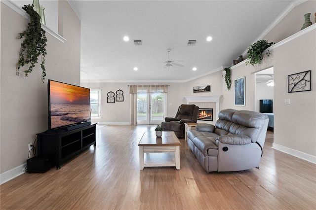 living room with ceiling fan, ornamental molding, a fireplace, and light hardwood / wood-style flooring