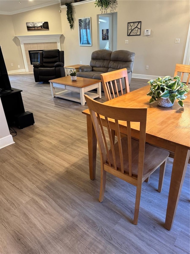 dining area featuring wood-type flooring, crown molding, and a tiled fireplace