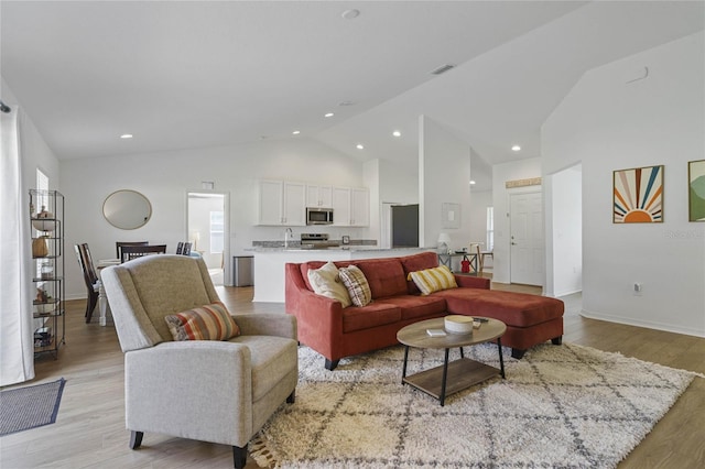 living room featuring light wood-type flooring, sink, and high vaulted ceiling