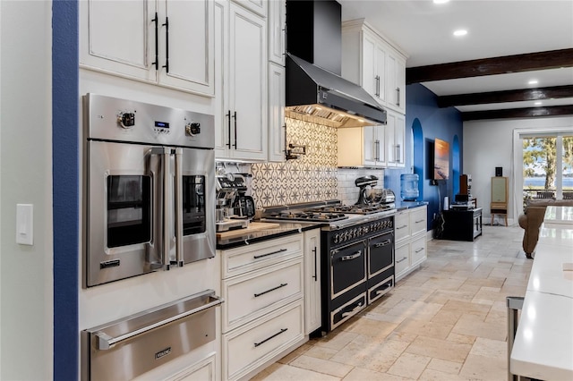 kitchen featuring tasteful backsplash, beam ceiling, white cabinetry, wall chimney exhaust hood, and double oven range