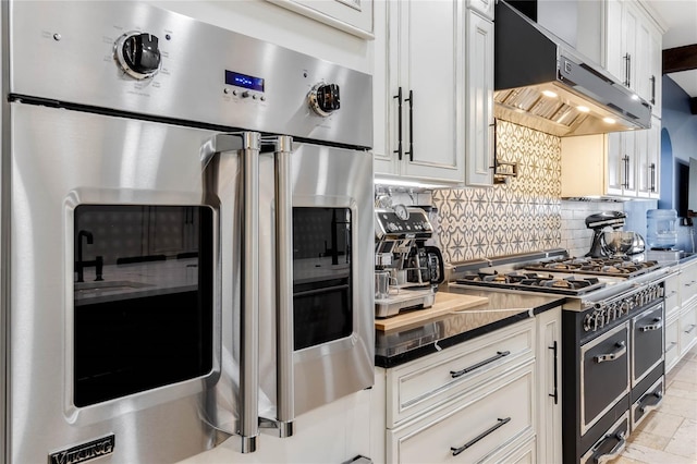 kitchen featuring dark stone countertops, white cabinetry, tasteful backsplash, double oven range, and extractor fan