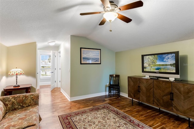 living room with a textured ceiling, lofted ceiling, ceiling fan, and dark wood-type flooring