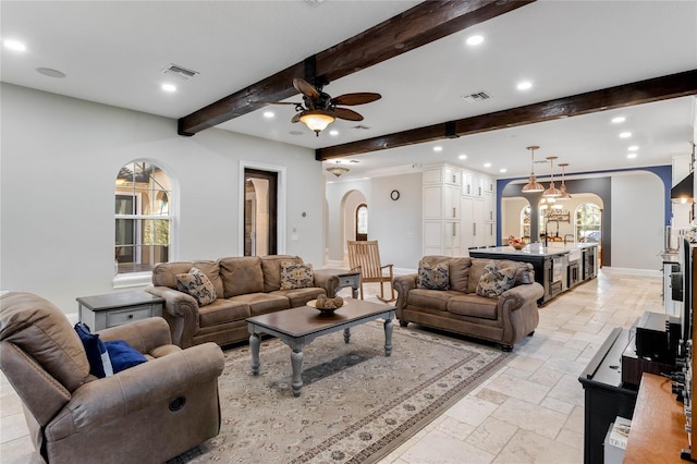 living room with ceiling fan with notable chandelier, beamed ceiling, and plenty of natural light