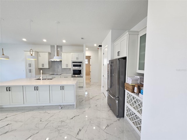 kitchen with stainless steel appliances, wall chimney range hood, white cabinets, and hanging light fixtures