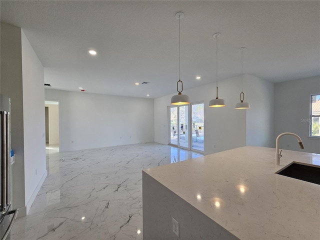 kitchen featuring light stone counters, a textured ceiling, hanging light fixtures, sink, and an island with sink