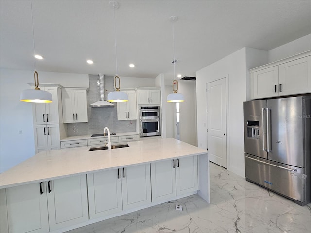 kitchen with stainless steel appliances, white cabinetry, wall chimney range hood, decorative light fixtures, and a large island with sink