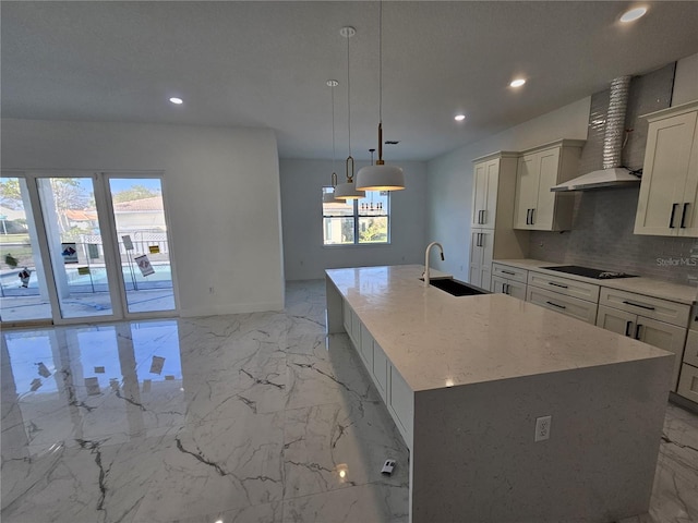 kitchen with light stone counters, wall chimney range hood, a large island with sink, hanging light fixtures, and sink