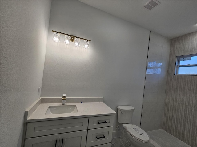 bathroom featuring a tile shower, vanity, and toilet