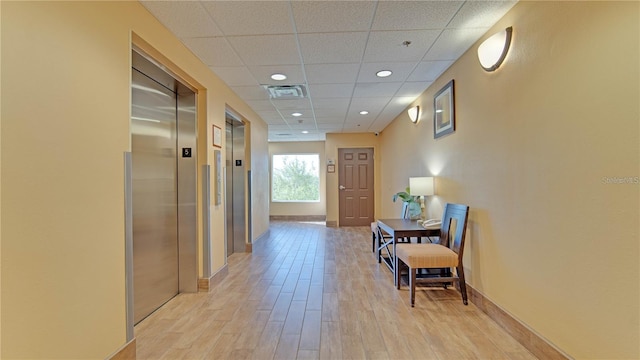 corridor featuring a drop ceiling, light hardwood / wood-style floors, and elevator