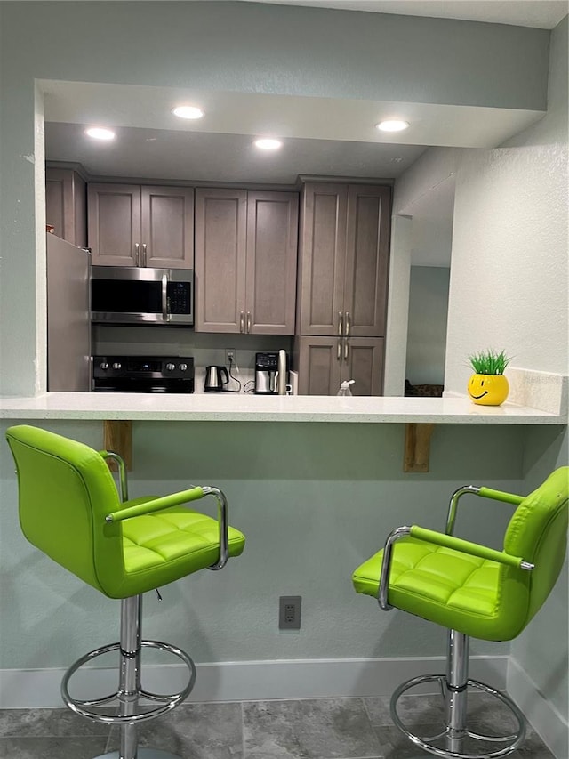 kitchen featuring stainless steel appliances, a kitchen breakfast bar, kitchen peninsula, and dark brown cabinets