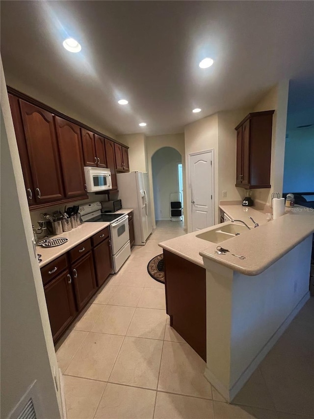 kitchen with sink, light tile patterned floors, kitchen peninsula, dark brown cabinets, and white appliances