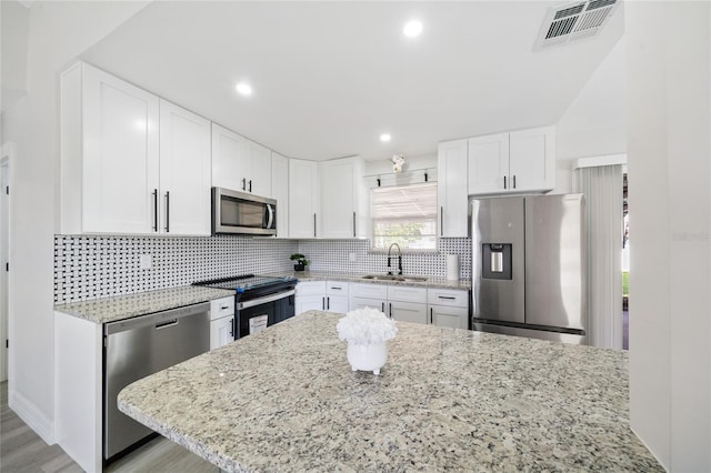 kitchen with light stone counters, sink, light hardwood / wood-style flooring, white cabinetry, and stainless steel appliances