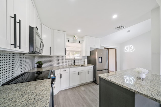 kitchen featuring light wood-type flooring, hanging light fixtures, stainless steel appliances, and white cabinets