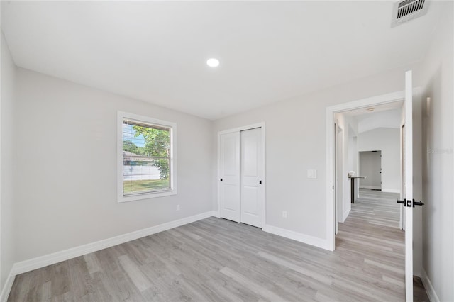 unfurnished bedroom featuring a closet, light hardwood / wood-style floors, and lofted ceiling