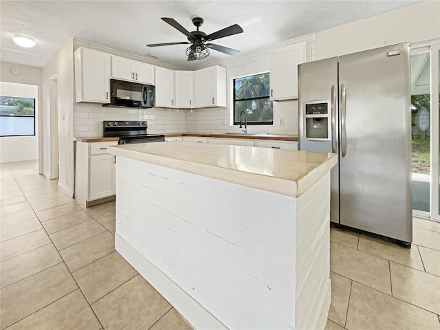 kitchen with appliances with stainless steel finishes, light tile patterned flooring, white cabinetry, backsplash, and a kitchen island