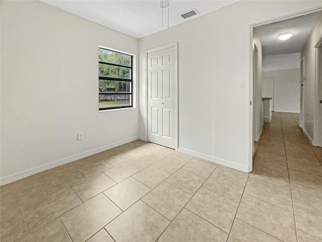 unfurnished bedroom featuring a textured ceiling, light tile patterned flooring, ceiling fan, and a closet