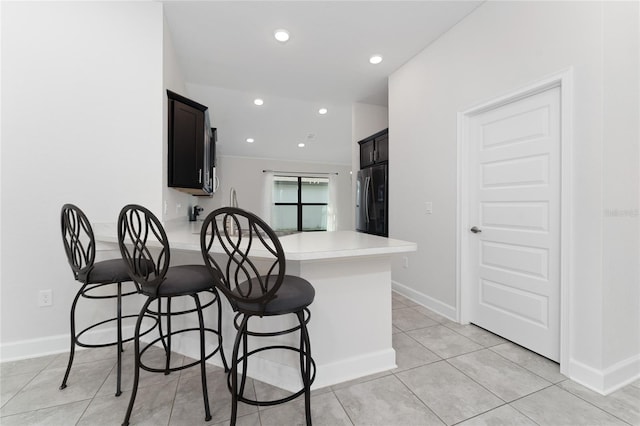 kitchen with a breakfast bar, kitchen peninsula, light tile patterned flooring, and stainless steel fridge