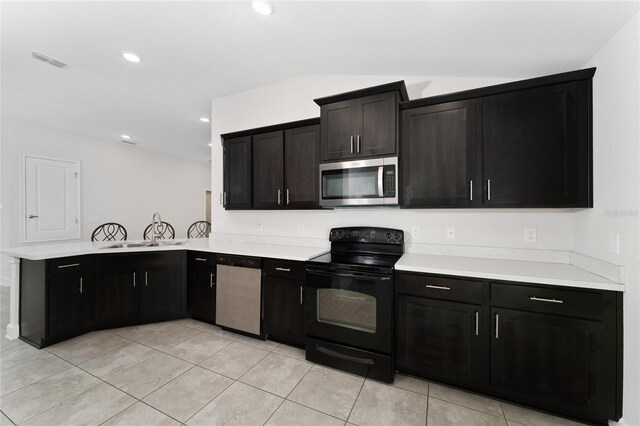 kitchen with sink, vaulted ceiling, kitchen peninsula, appliances with stainless steel finishes, and light tile patterned floors