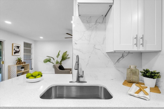 kitchen featuring light stone countertops, white cabinets, and sink