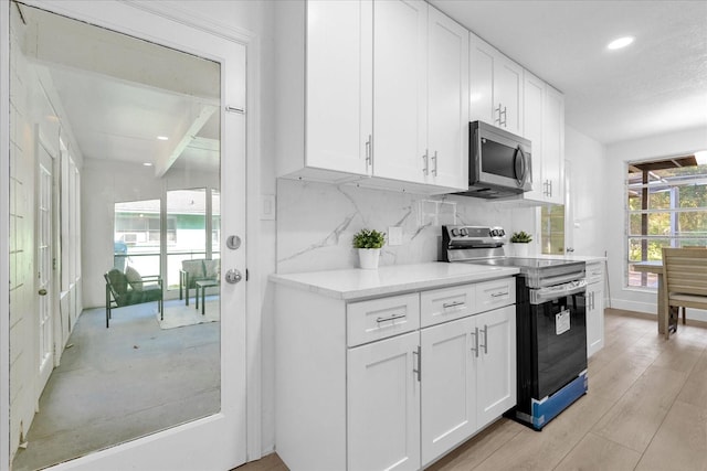 kitchen with decorative backsplash, white cabinetry, light hardwood / wood-style floors, and appliances with stainless steel finishes