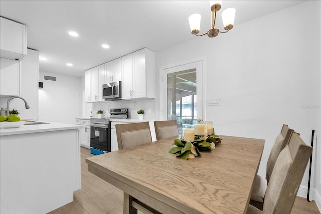 dining room with light wood-type flooring, sink, and a chandelier