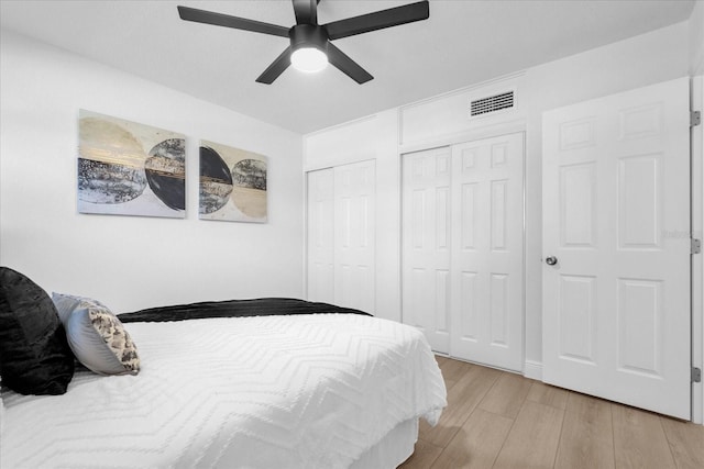 bedroom with ceiling fan, multiple closets, and light hardwood / wood-style flooring