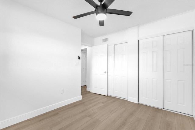 unfurnished bedroom featuring light wood-type flooring, two closets, and ceiling fan