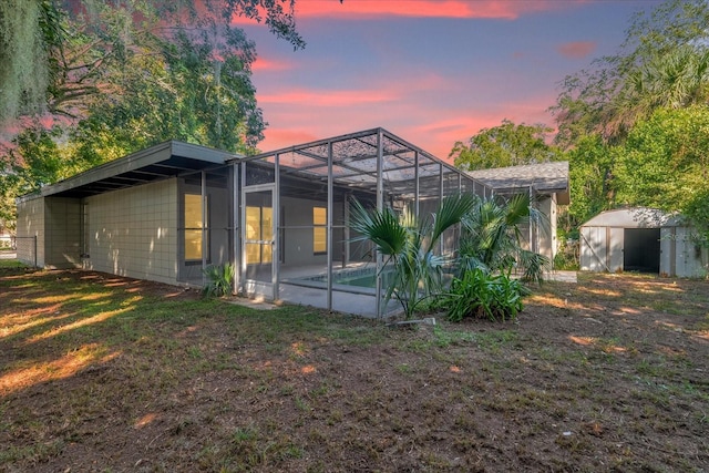 back house at dusk featuring a patio, a storage shed, and a lanai