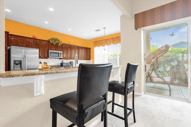 kitchen with a kitchen breakfast bar, light carpet, decorative light fixtures, backsplash, and appliances with stainless steel finishes